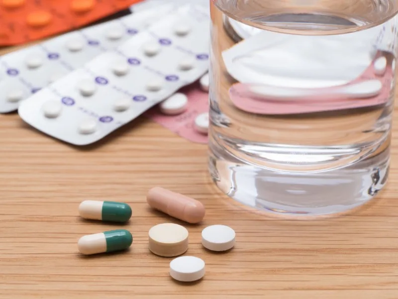 Various pills and a glass of water on wood