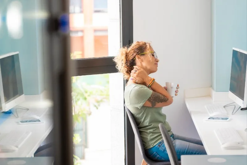 Woman sitting at desk rubbing neck