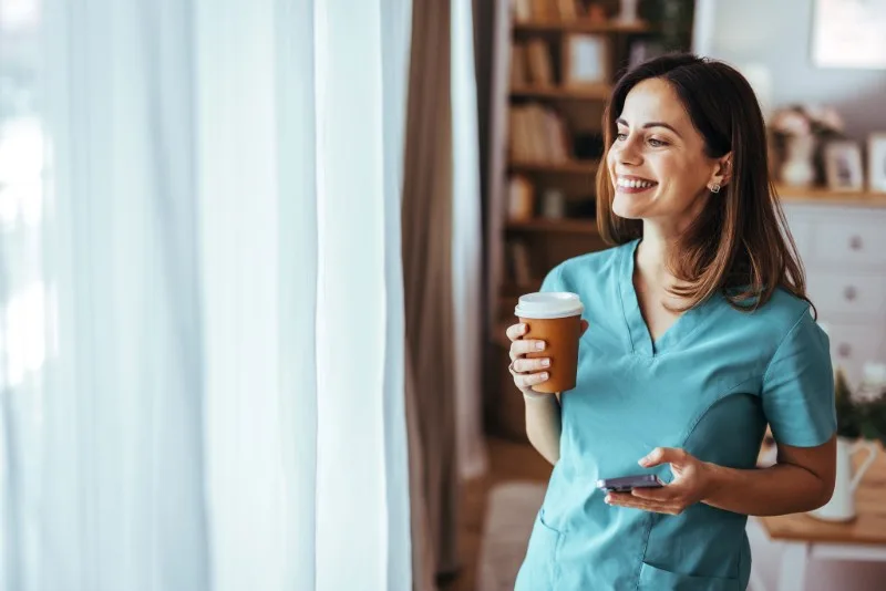 Woman in scrubs holding coffee and phone