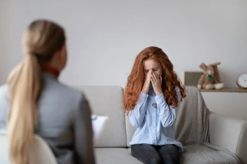 Teenager covering face while seated on sofa
