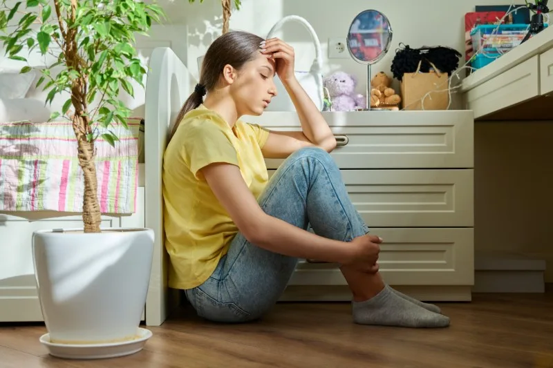 Teenager sitting on bedroom floor looking down