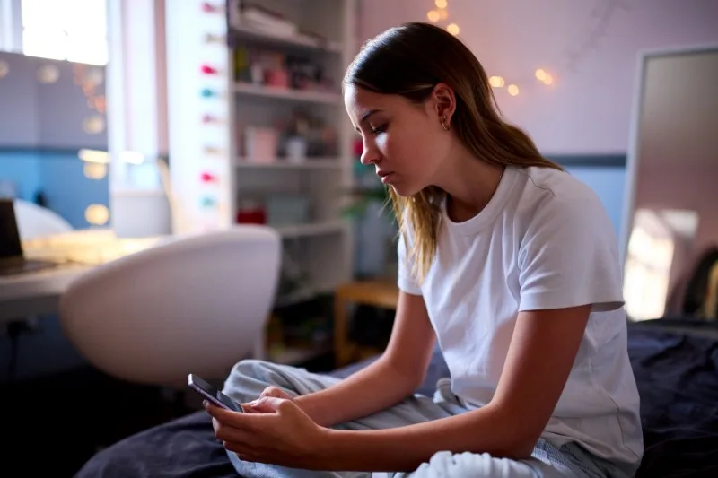 teenager sitting on bed looking at hands
