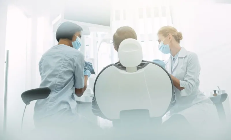 Dental patient in chair with two masked clinicians