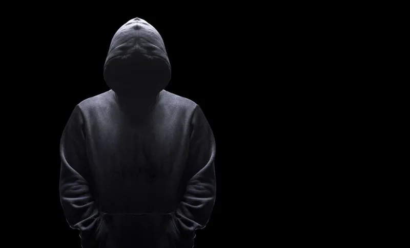 Hooded figure standing against black background