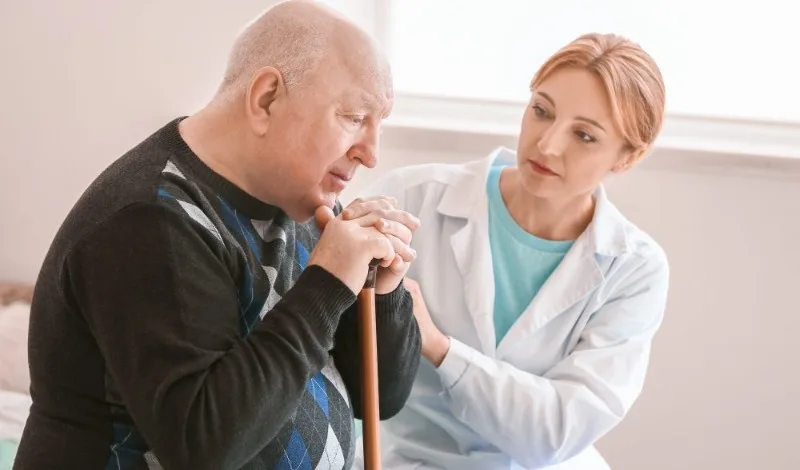 Caregiver speaking with an elderly man holding a cane