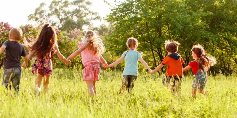 Children holding hands walking through grassy field