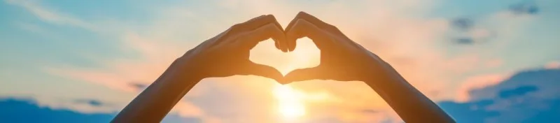 Hands forming heart shape at sunrise