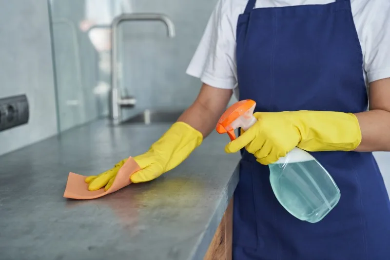 Person wiping countertop with unlabelled spray and cloth