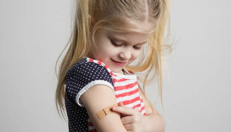 Young girl showing adhesive bandage on upper arm after vaccination